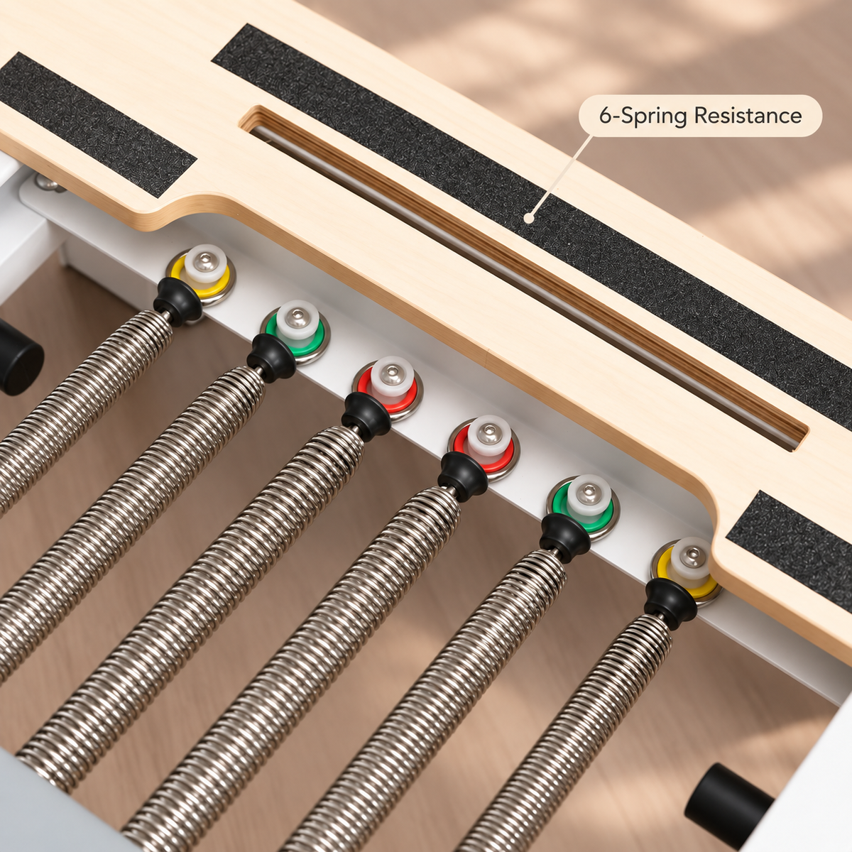 Close-up of six colour-coded resistance springs beneath the wooden platform of the aluminium Pilates reformer